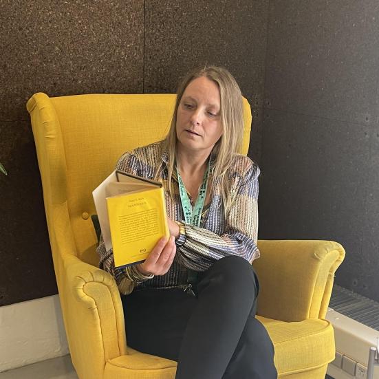 Nina sidder i en gul stol og læser i en bog.