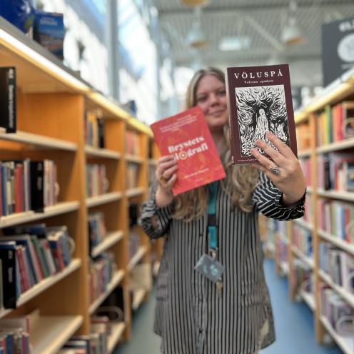 Sørine står blandt fyldte bogreoler, hvor hun i hænderne holder de omtalte bøger i denne artikel. Hun holder "Völuspá" frem for sig, så der er fokus på denne bogs forside. Både Sørine og baggrunden er let slørret.