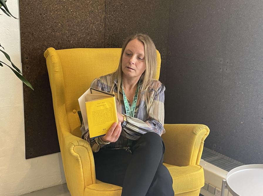 Nina sidder i en gul stol og læser i en bog.