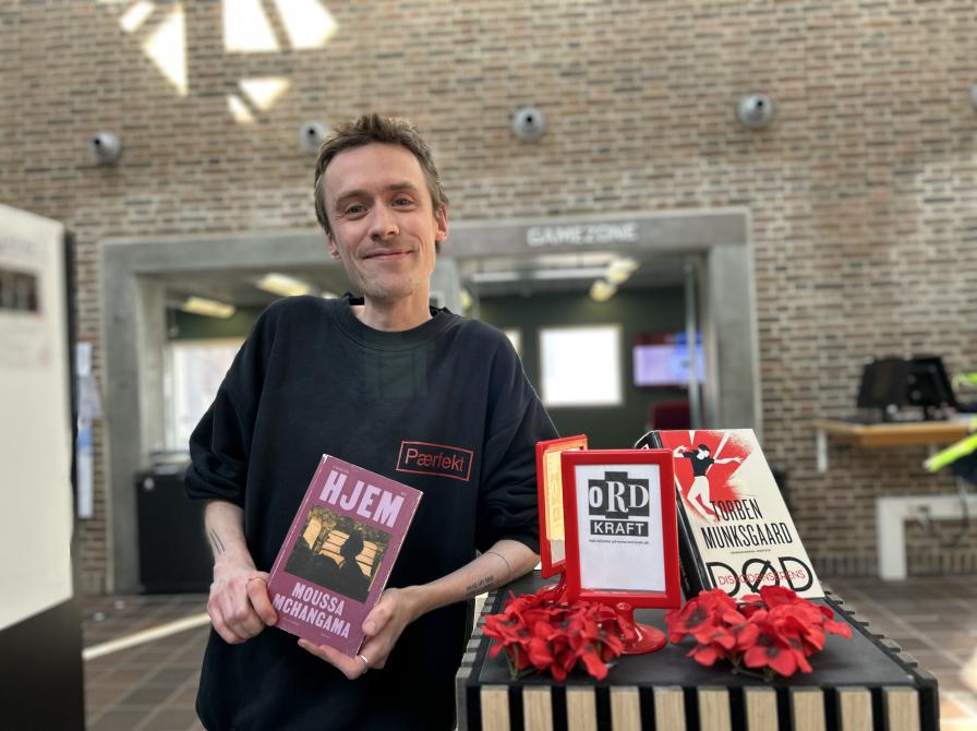 Søren Malthe står ved siden af Ordkraft-udstillingen på Hovedbiblioteket. Han holder den omtalte bog i denne artikel mellem hænderne og smiler let til kameraet. Baggrunden er let sløret og viser biblioteksrummet med bl.a. Gamezone.